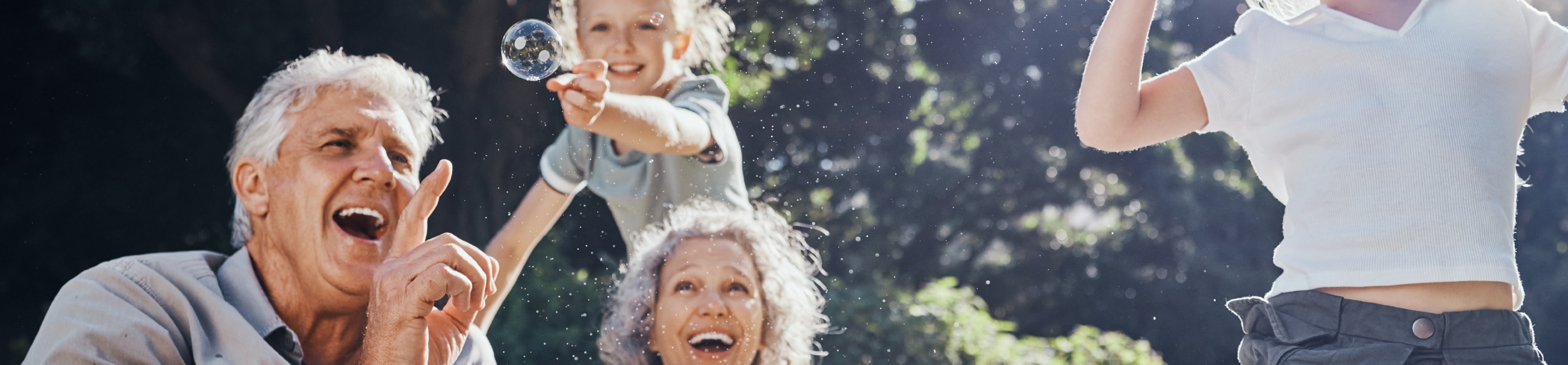 grandparents & children outside laughing & playing with bubbles