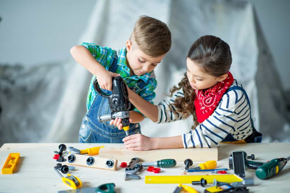 little boy and girl use a play drill with a table full of tools