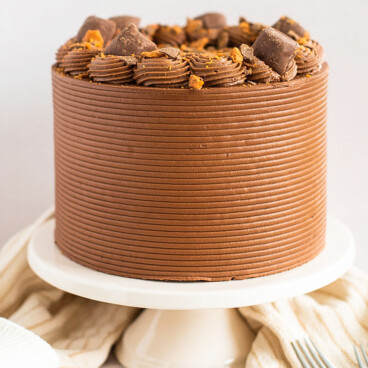 A chocolate peanut butter Butterfinger Cake on a cake stand.