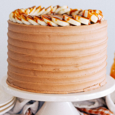 A decorated cake on a cake stand decorated with bananas and caramel.