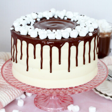 Cake on a cake stand with a chocolate drip and marshmallows on it.