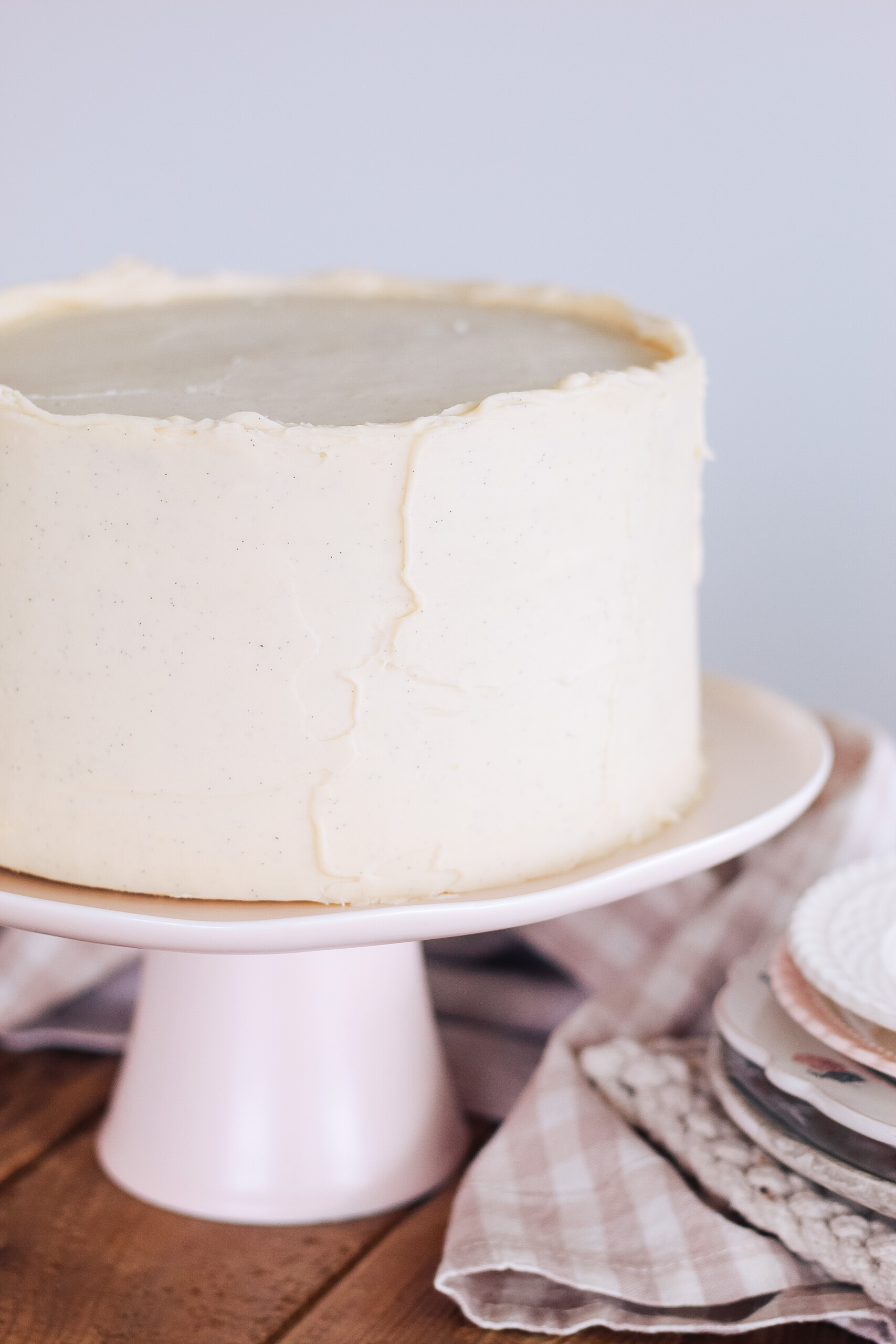 Cream cheese frosting covered cake on a cake stand with plates next to it.