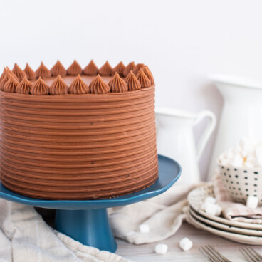 Chocolate cake on a blue cake stand with plates next to it.