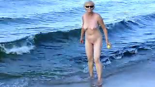 Naked old woman playing and having fun on the beach